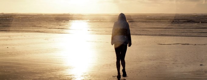 a woman walking on the beach at sunset